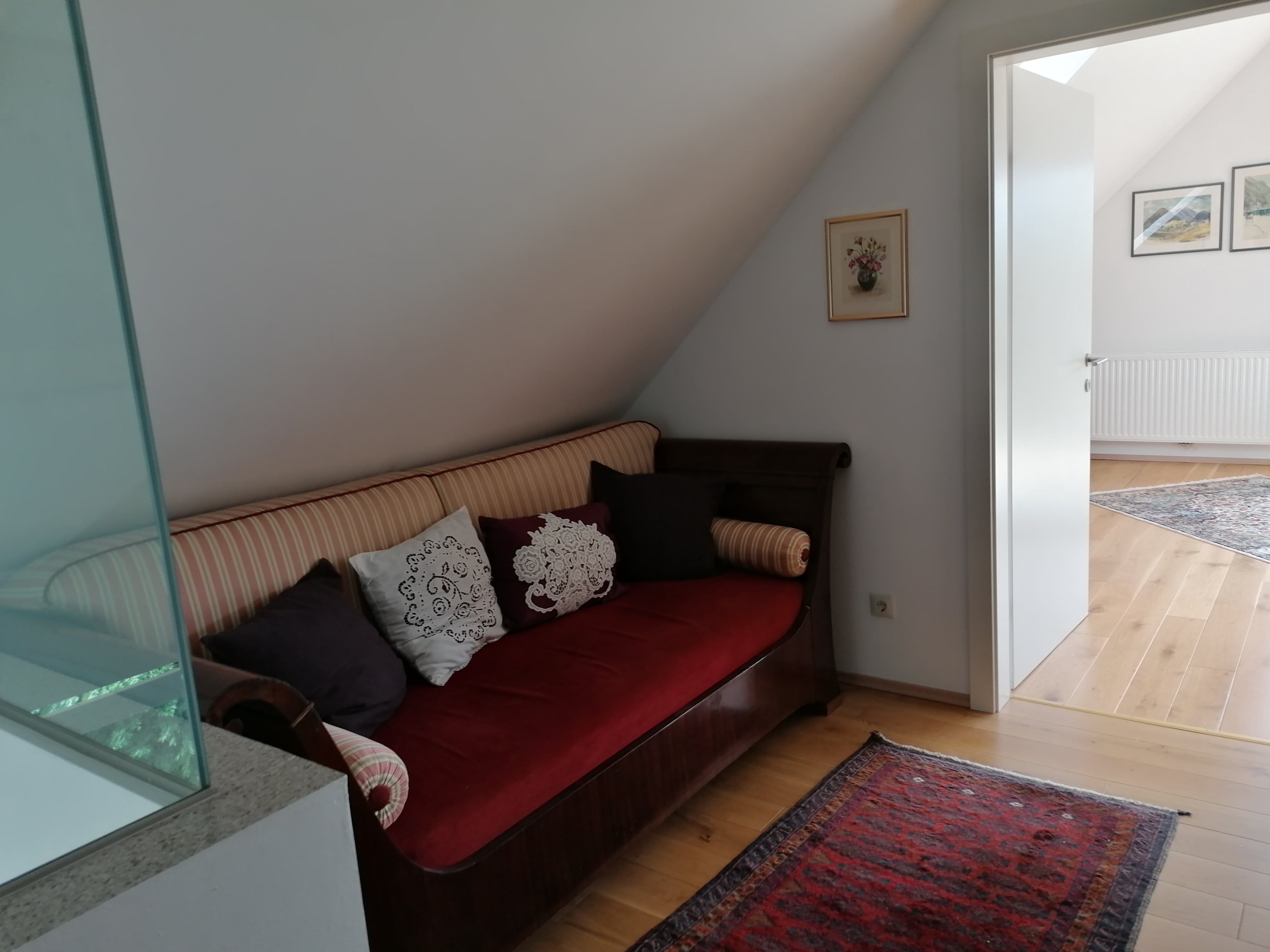 Ein Sofa mit Kissen steht in einem Flur vor einer offenen Tür zu einem hellen Raum.