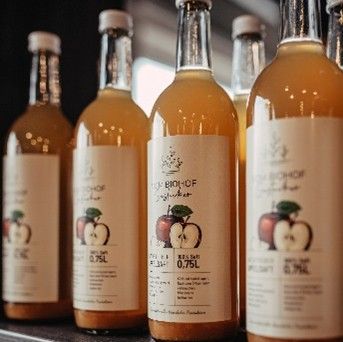 Mehrere Flaschen mit trübem Apfelsaft oder Apfelmost stehen nebeneinander, im Vordergrund eine Flasche mit Etikett und 0,75 l Angabe.