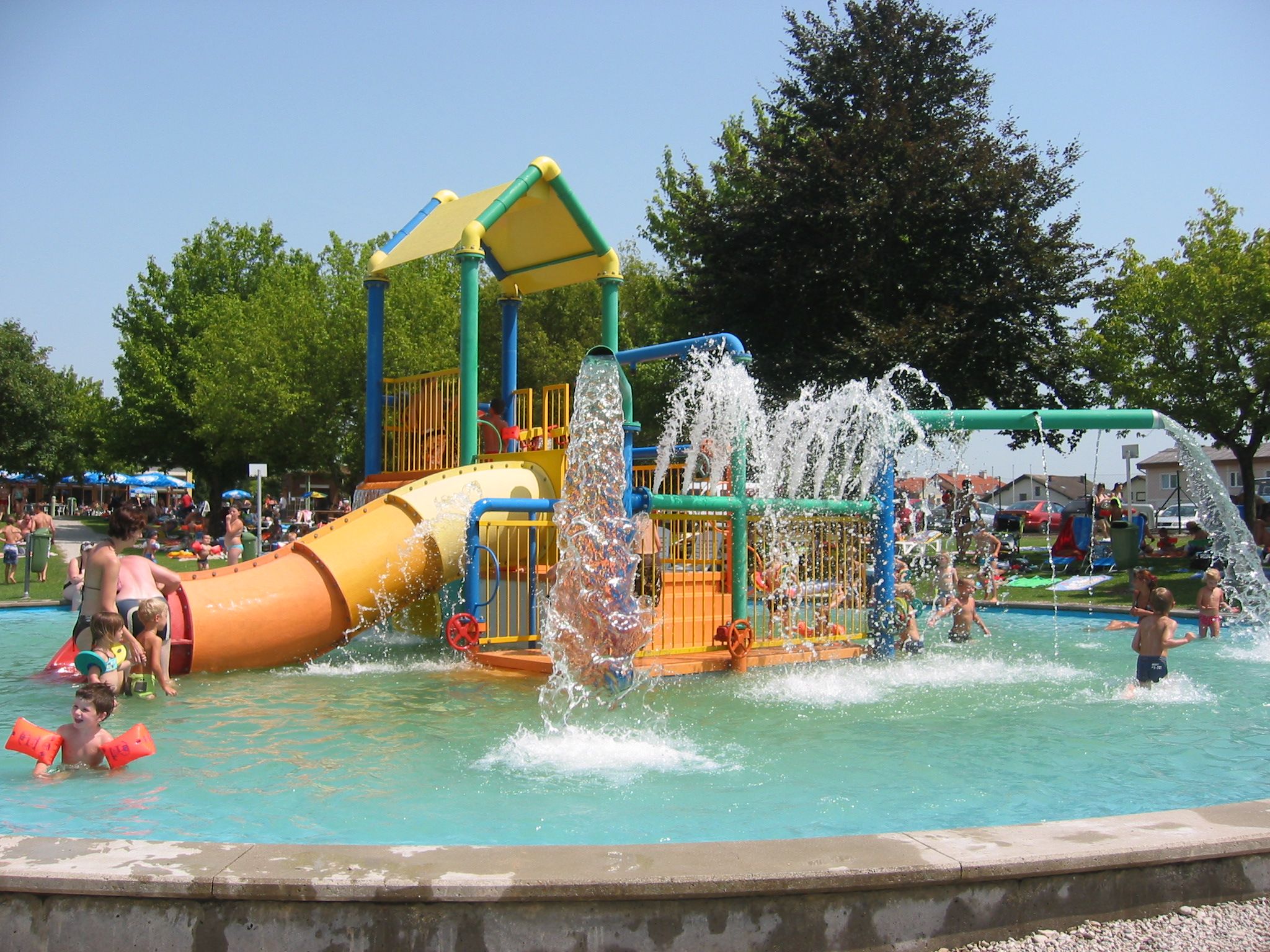Kinder spielen in einem Wasserspielgarten mit Rutschen und Wasserfontänen.