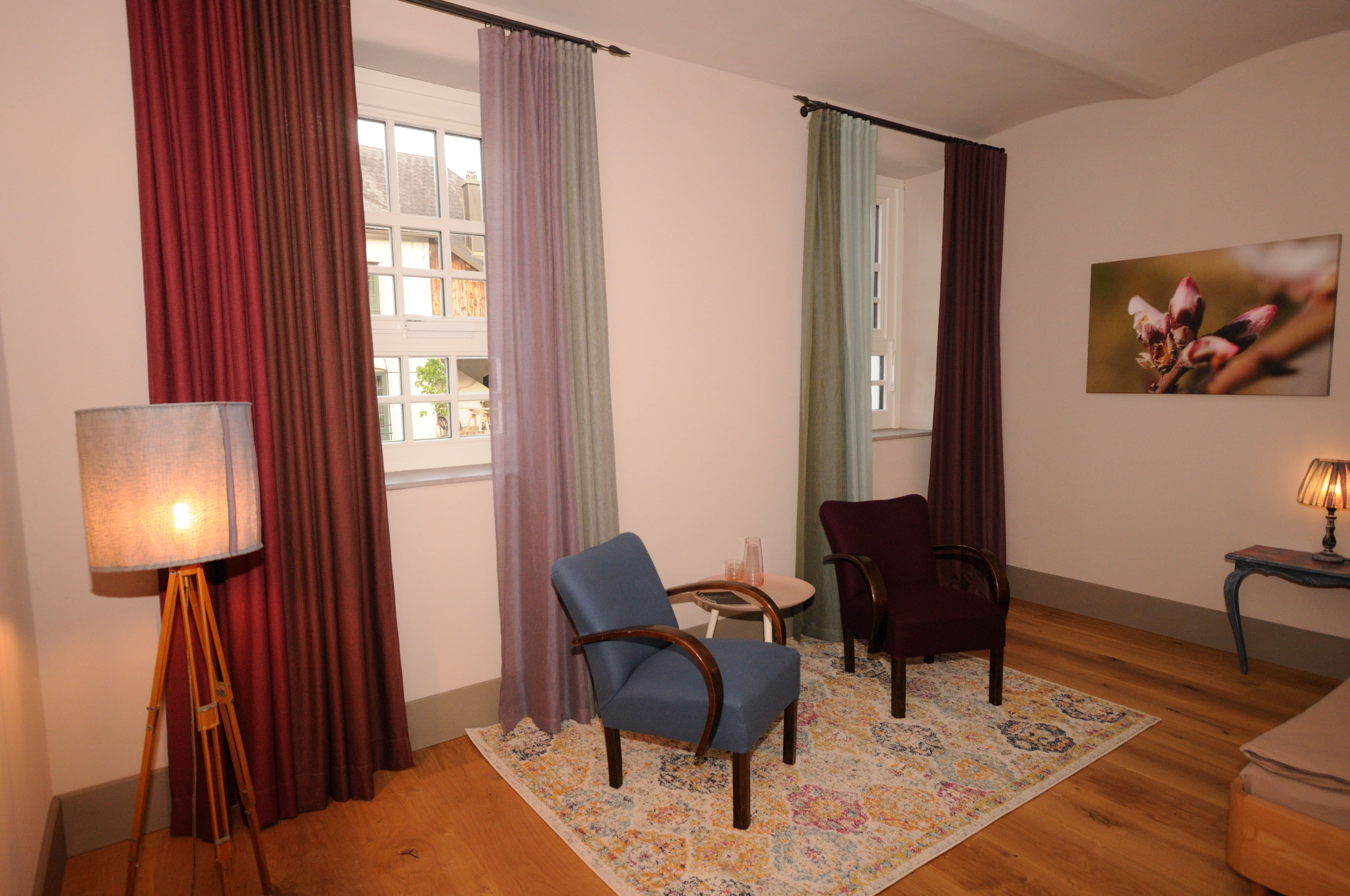 Gemütliches Zimmer mit zwei Sesseln, bunten Vorhängen und einem Teppich.