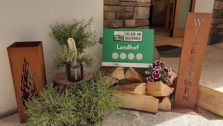 Eingangsbereich mit Holzscheiten und einem Willkommensschild.