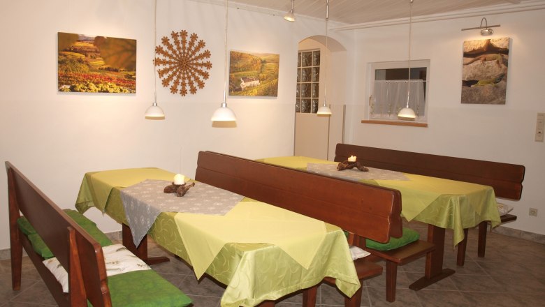 Ein gemütlicher Frühstücksraum mit Holzbänken, grünen Tischdecken und Wanddekorationen.