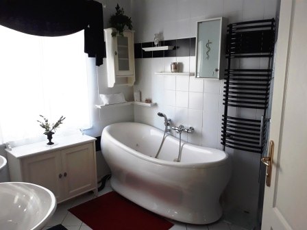 Modernes Badezimmer mit freistehender Badewanne, wei&szlig; gefliest, schwarzer Handtuchhalter und roter Teppich.