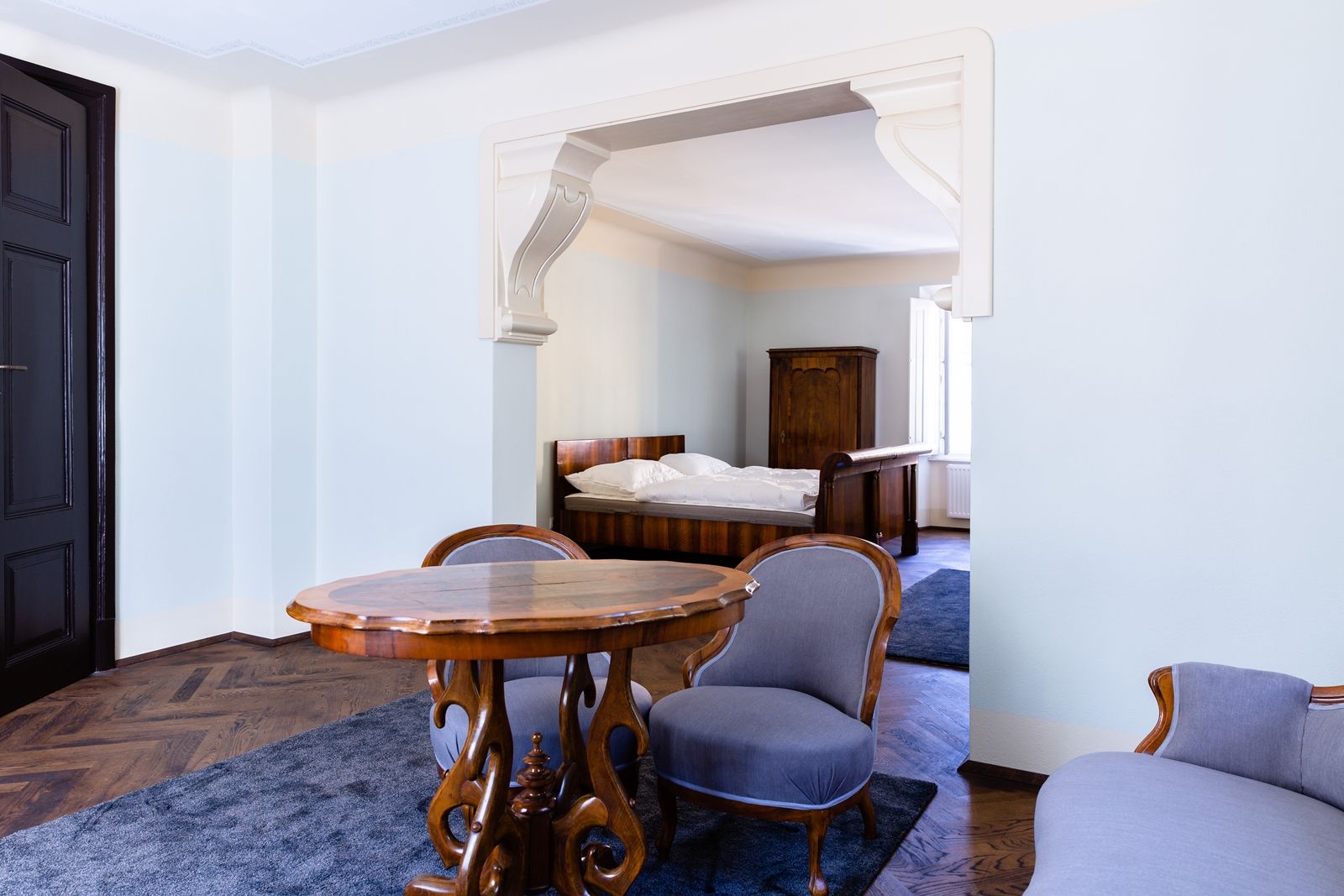 Ein elegantes Zimmer mit antiken Möbeln, darunter ein Holztisch, zwei Stühle und ein Bett im Hintergrund.