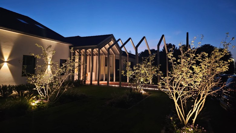 Beleuchtetes Geb&auml;ude bei Nacht mit modernen Strukturen und B&auml;umen im Vordergrund.