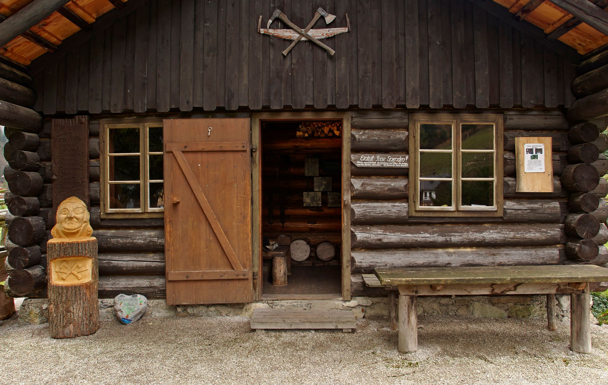 Eine rustikale Holzhütte mit offener Tür, Holzschnitzerei und Tisch davor.