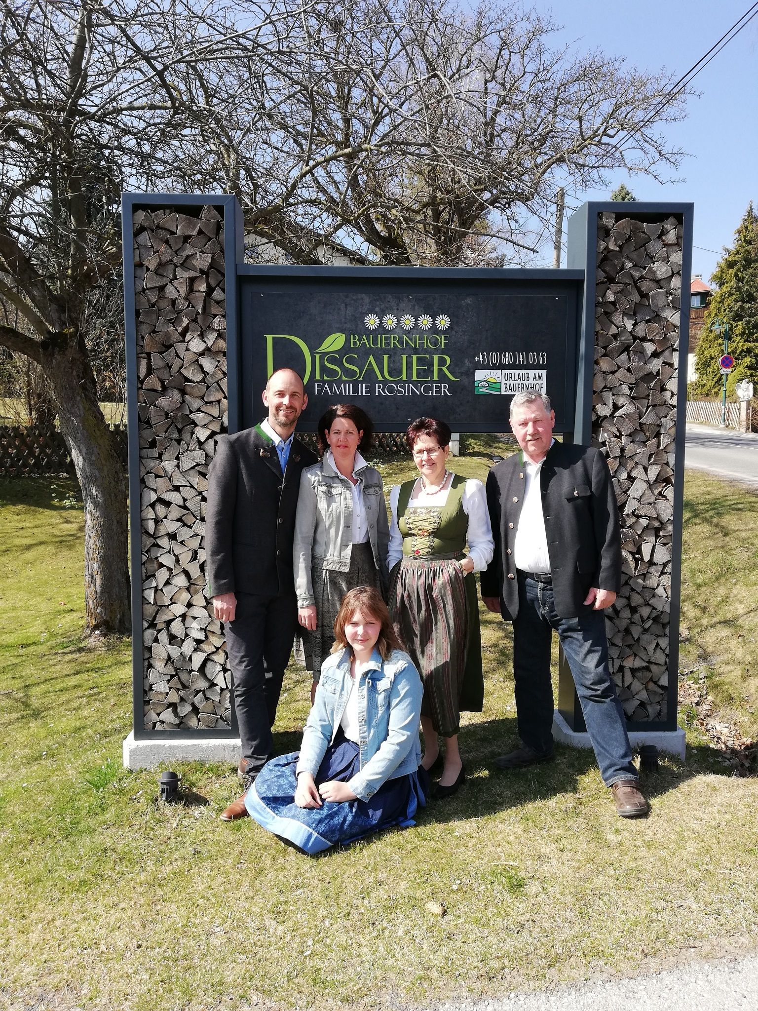 Fünf Personen vor einem Schild mit der Aufschrift 'Bauernhof Dissauer Familie Rosinger'.