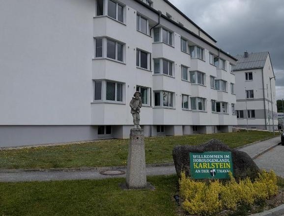 Ein modernes, wei&szlig;es Geb&auml;ude mit mehreren Stockwerken und einem Schild mit der Aufschrift 'Willkommen im Horologenland Karlstein an der Thaya'.
