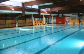 Innenansicht eines Schwimmbads mit leeren Liegestühlen am Beckenrand.