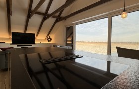 Moderner Wohn- und Essbereich mit Holzbalken, Kochinsel und großem Fenster mit Ausblick.