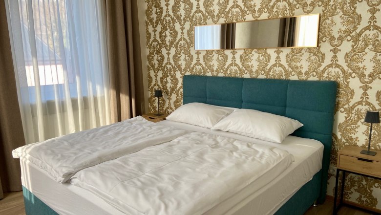 Ein stilvoll eingerichtetes Schlafzimmer mit einem großen Bett, blauen Kopfteil und goldener Tapete.