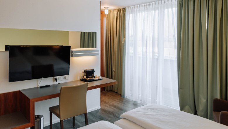 Modernes Hotelzimmer mit Schreibtisch, Fernseher und Vorh&auml;ngen.