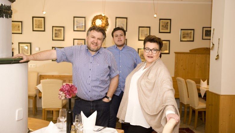 Die Gastgeberfamilie in einem Restaurant, lächelnd in die Kamera schauend. Der Raum ist mit Bildern und einem Kranz dekoriert.