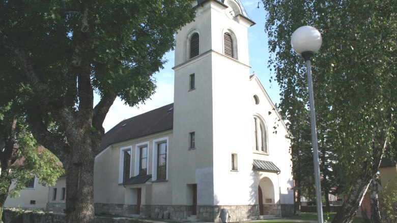 Kirche in Pischelsdorf mit Turm und B&auml;umen im Vordergrund.