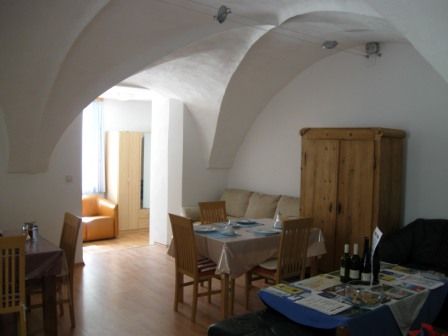 Ein Wohnzimmer mit Gewölbedecke, Esstisch, Stühlen und einem Schrank.