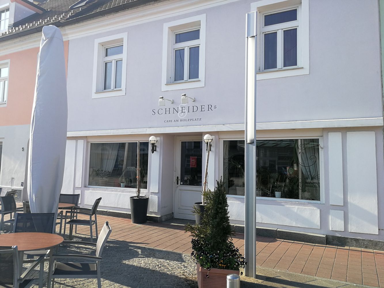 Außenansicht eines Cafés mit Terrasse und Sonnenschirm.