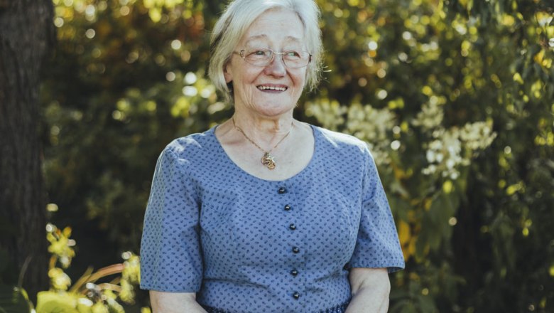 &Auml;ltere Frau in blauer Kleidung l&auml;chelt im Freien.