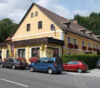 Ein gelbes Gasthaus mit roten Blumen und parkenden Autos davor.