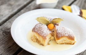 Drei Buchteln mit Puderzucker und Physalis auf Vanillesauce auf einem wei&szlig;en Teller.