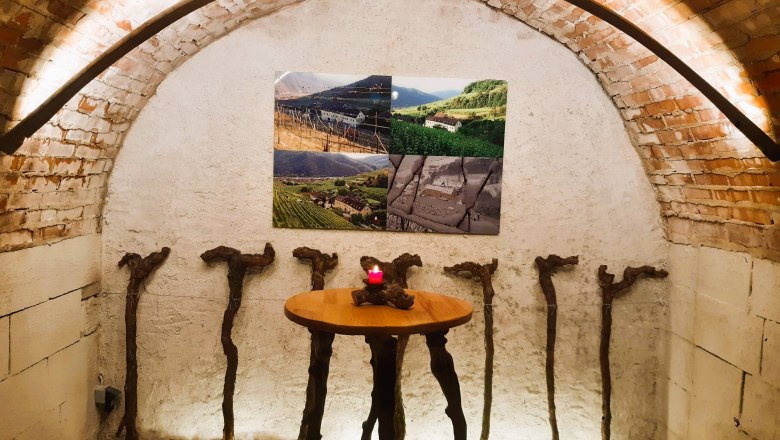 Gewölbter Weinkeller mit Tisch und Weinreben-Dekoration.