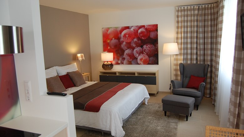 Apartment Zweigelt, © Harald Hundskarl Modern eingerichtetes Schlafzimmer mit Doppelbett, Sessel und großem Bild von Weintrauben an der Wand.