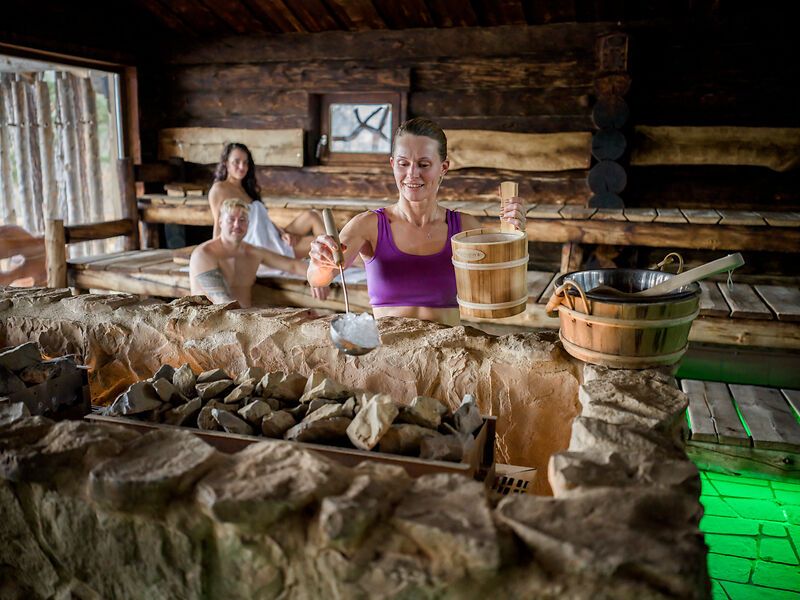 Person gießt Wasser auf heiße Steine in einer Sauna.