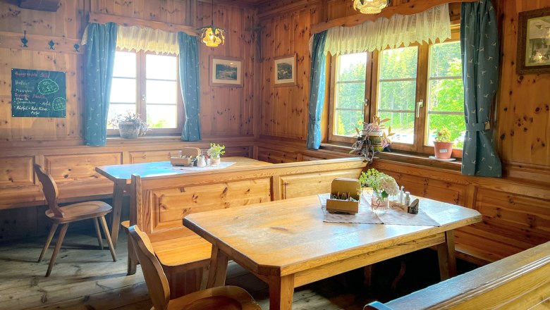 Gemütliche Stube mit Holzmöbeln, blauen Vorhängen und Pflanzen auf den Tischen.