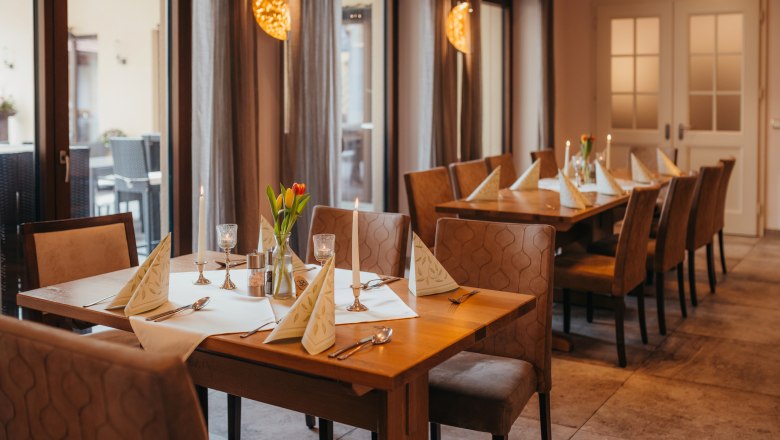 Ein gem&uuml;tlich gedeckter Tisch in einem Wirtshaus mit Kerzen und Blumen.