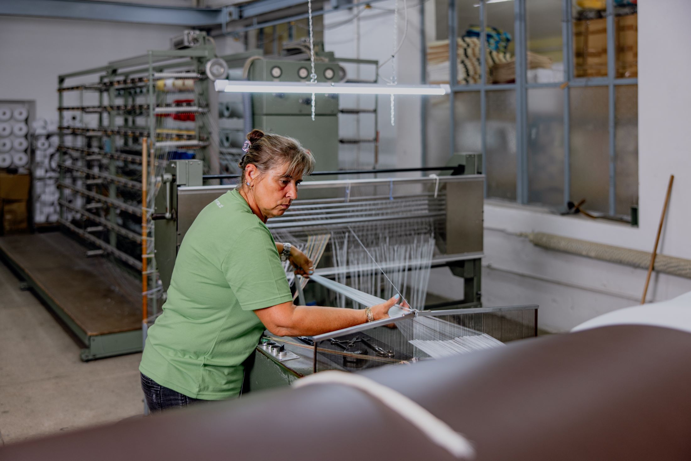 Frau arbeitet an einer Webmaschine in einer Textilfabrik.