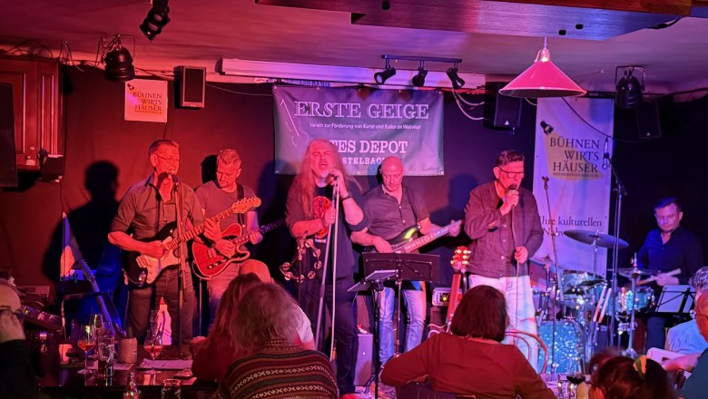 Band spielt auf einer Bühne in einem kleinen Veranstaltungsort mit Publikum.