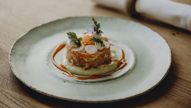 Gourmetgericht auf einem Teller mit Lachs, Kr&auml;utern und So&szlig;e dekoriert.