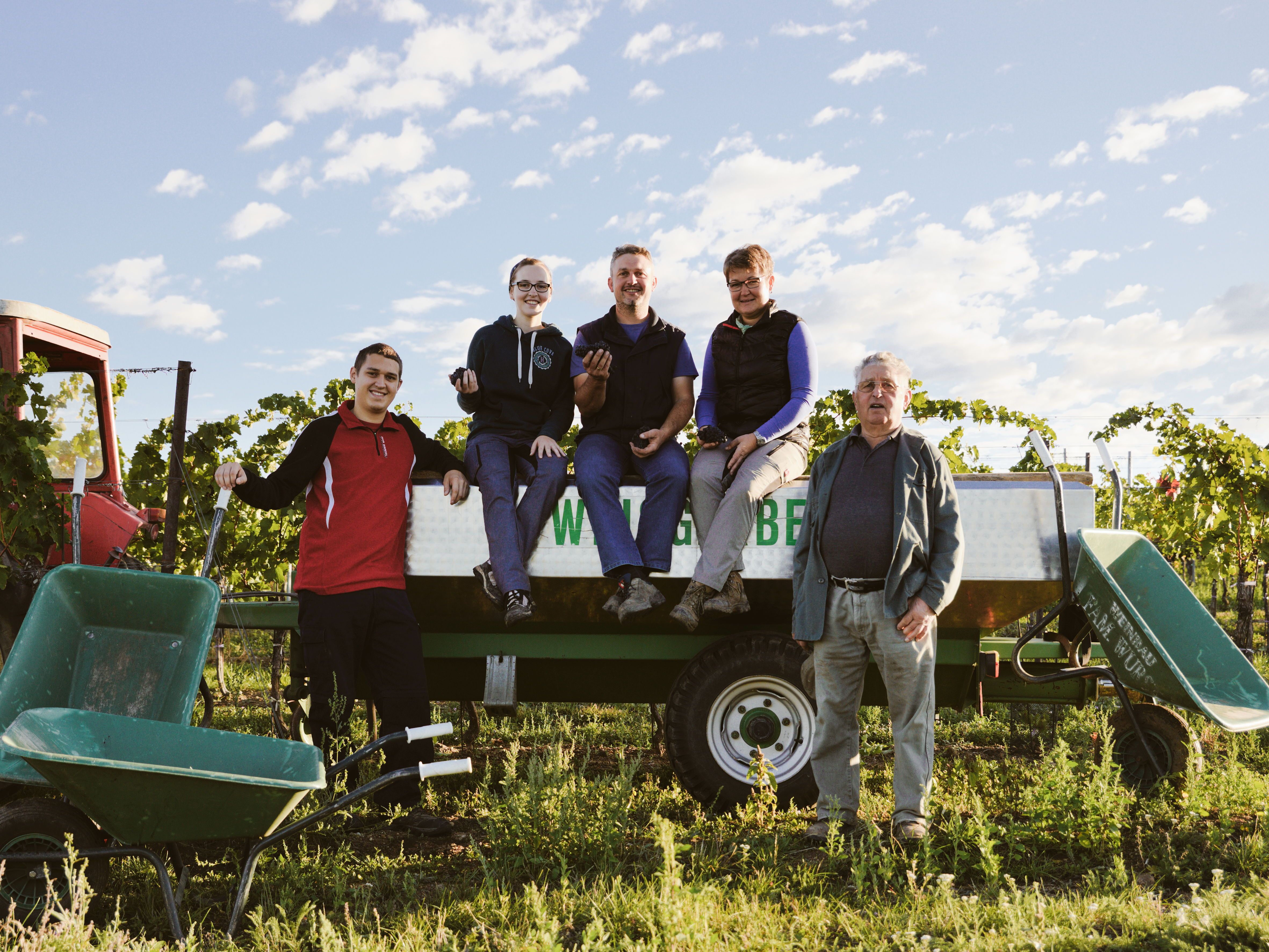Eine Familie posiert auf einem Traktoranhänger in einem Weinberg.