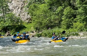 Personen beim Tubing auf einem Fluss in einer gr&uuml;nen, bewaldeten Umgebung.