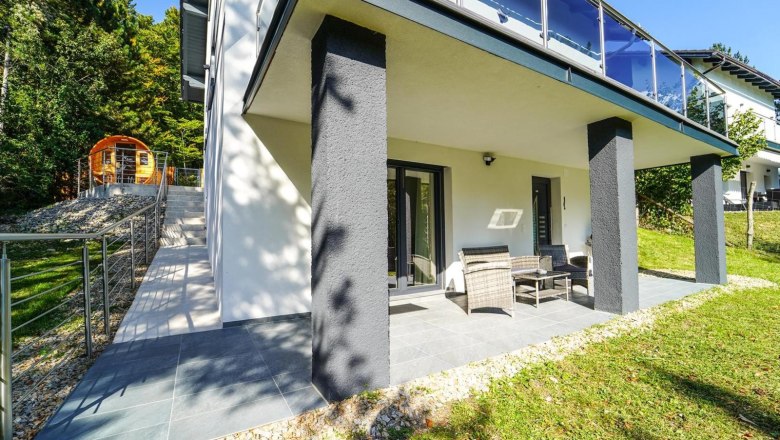 Terrasse eines modernen Ferienhauses mit Gartenmöbeln und angrenzendem Garten.